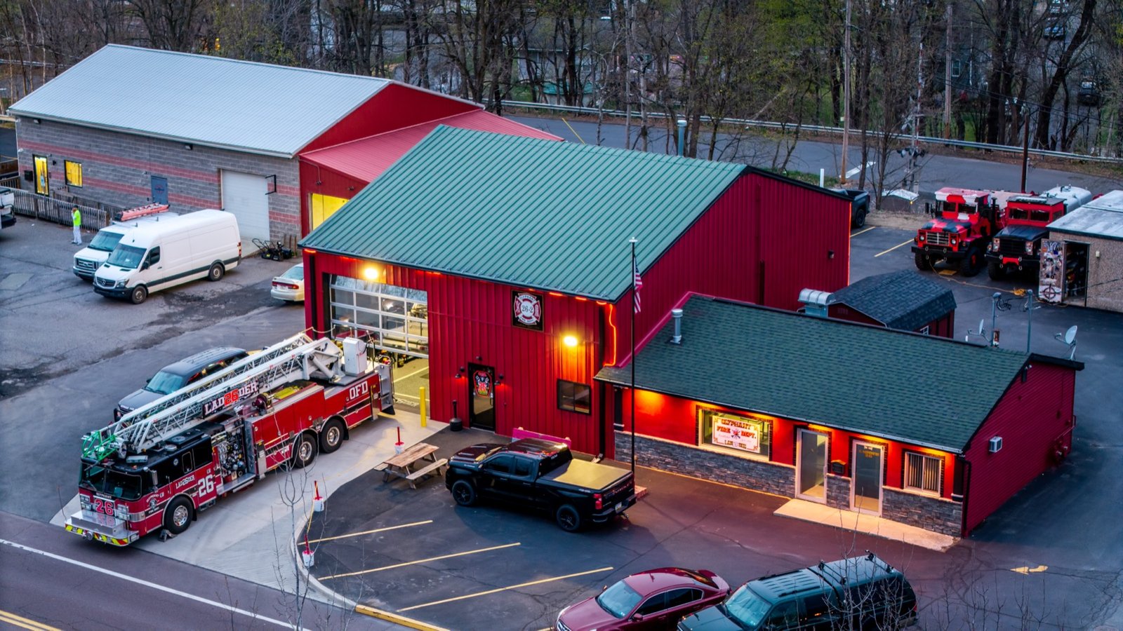 Red fire station at dusk with a ladder truck parked out front