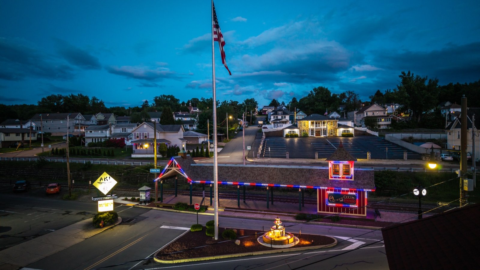 Flag, fountain and lit-up storefront at dusk