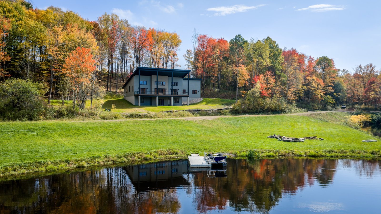 Newly built modern home above a private lake, with fall trees reflected in the water